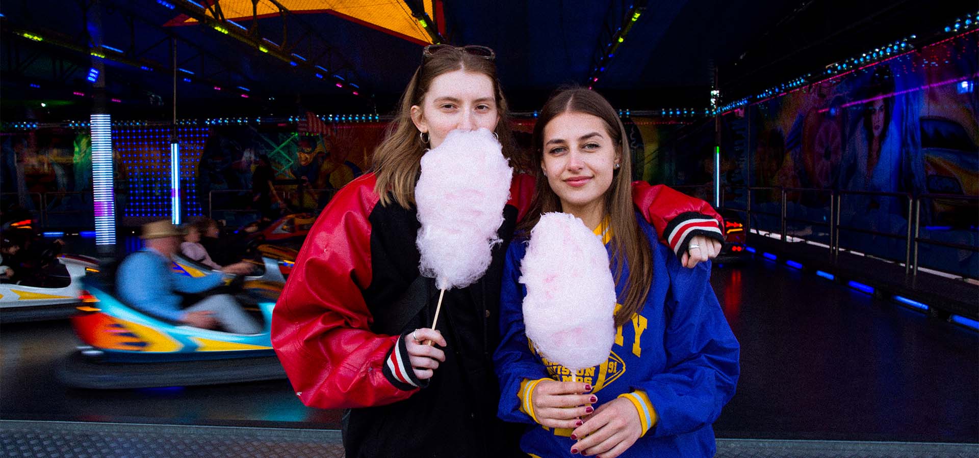 2 junge Frauen stehen vor einem Autoscooter mit Zuckerwatte